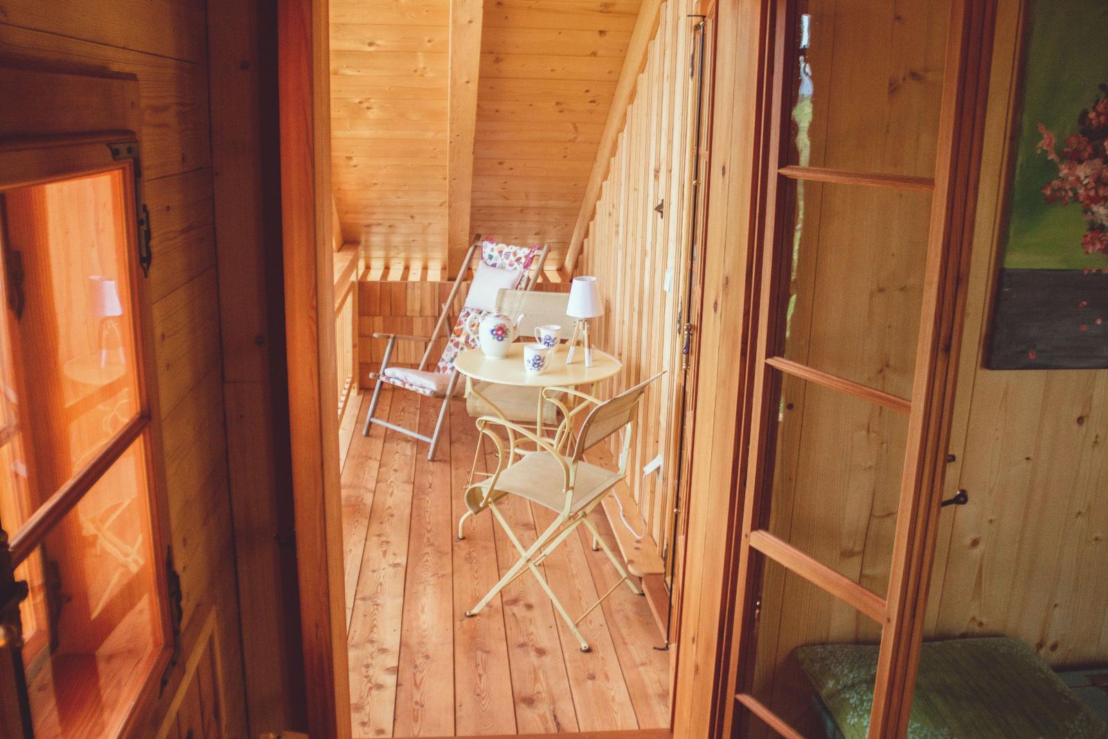 Hölzerner Balkon mit Tisch, Stühlen und Teeservice. Holzwände und Boden.