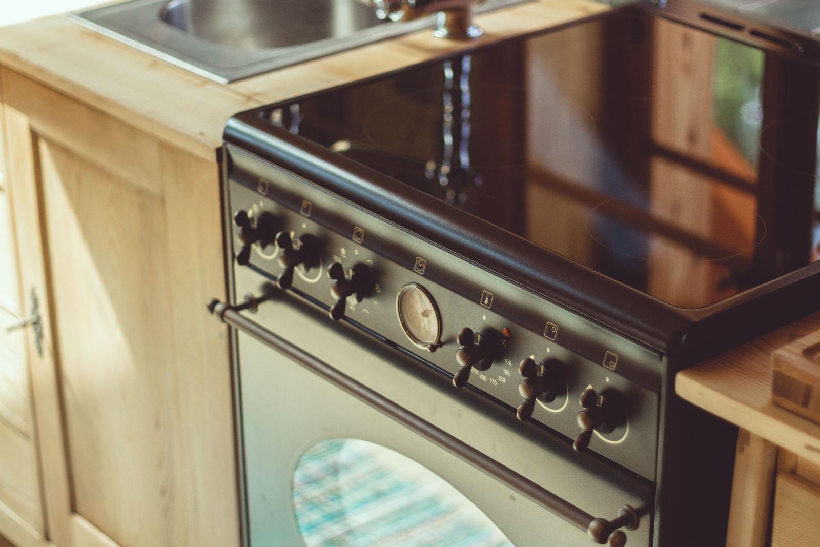 Küchenzeile mit schwarzer Kochplatte und Ofen, Holzoberflächen und Edelstahlwaschbecken.