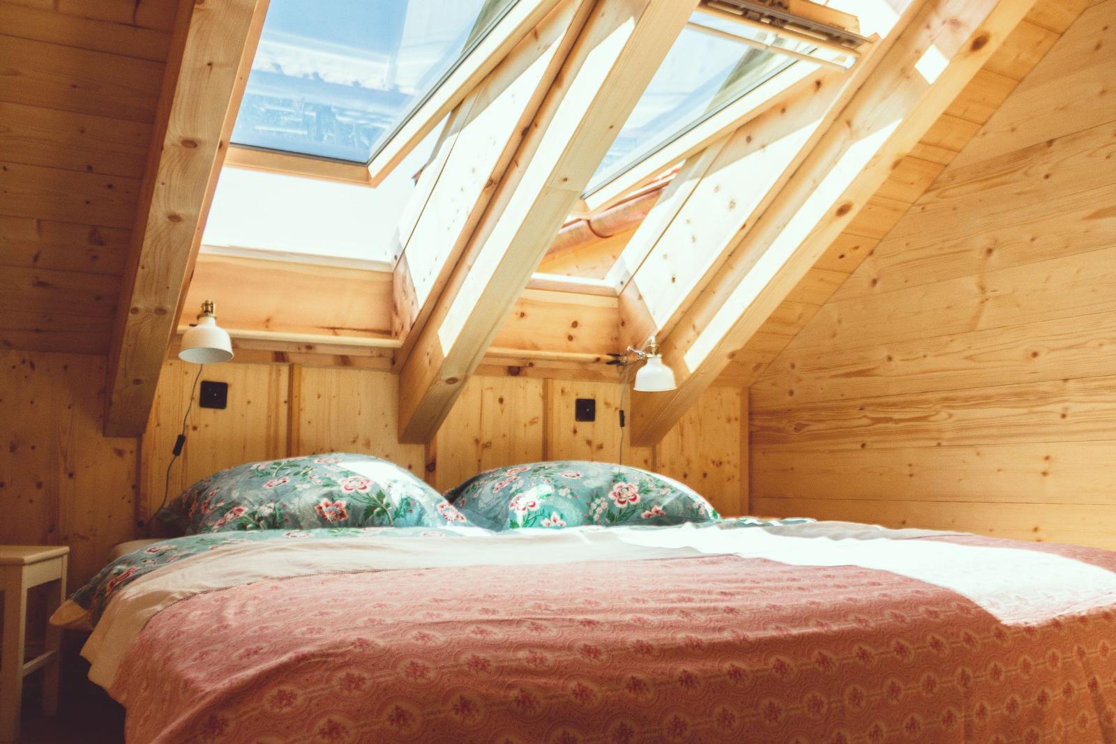 Doppelbett unter Dachschrägen mit Dachfenstern und Holzwänden.