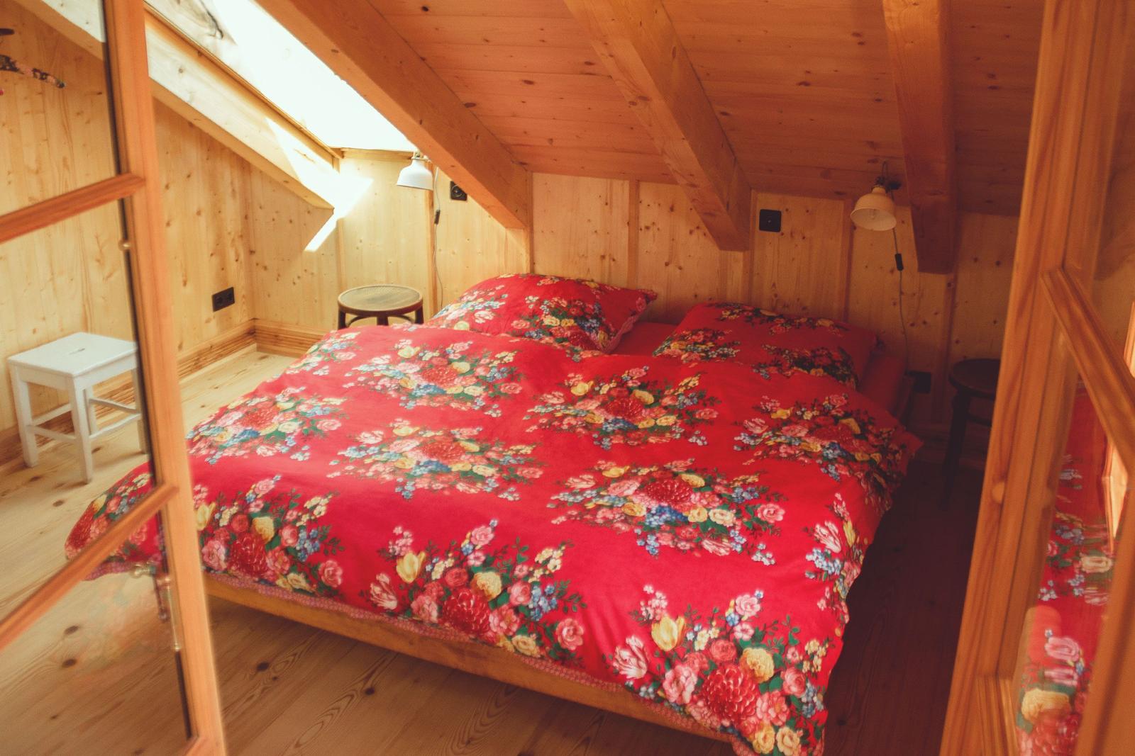 Schlafzimmer mit Holzwand, Dachboden und Bett mit blumigem Bettbezug.