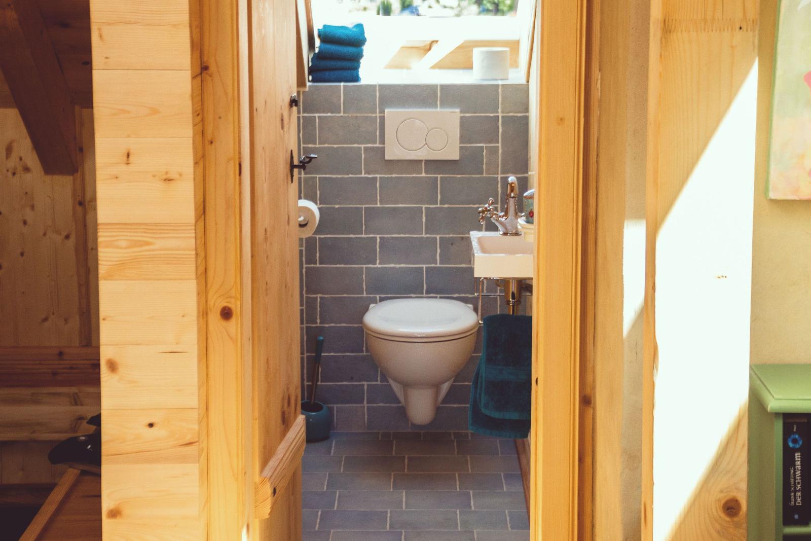 Badezimmer mit Toilette, Waschbecken und blauen Handtüchern an Holzwänden.