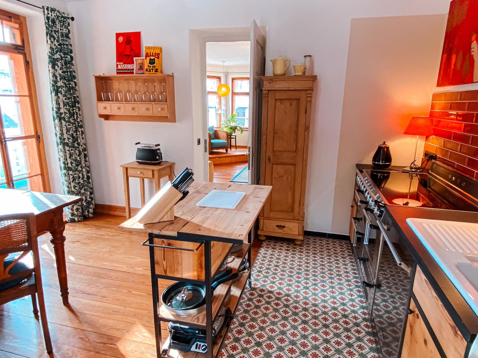 Küche mit Holzwerkzeug, Mosaikboden und Küchenspüle. Durchgang in Wohnzimmer mit Sofa.