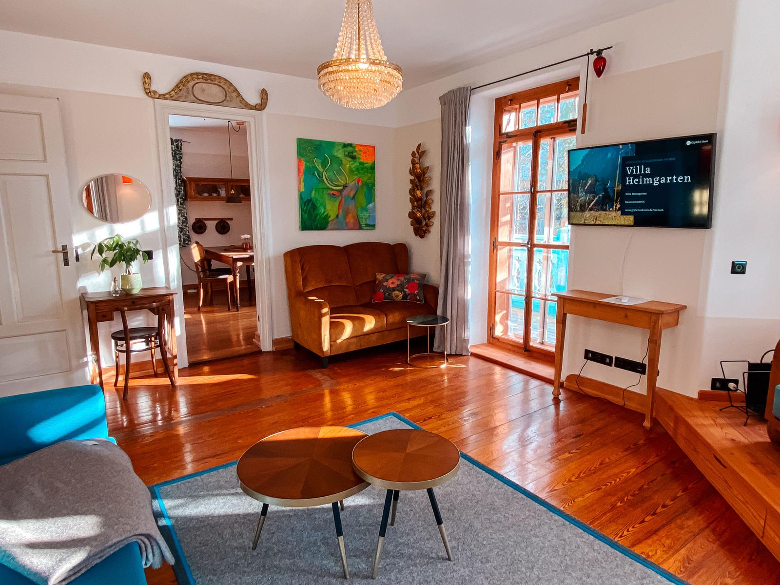 Wohnzimmer mit Holzboden, Sofa, Fernseher und Blick auf Balkon.