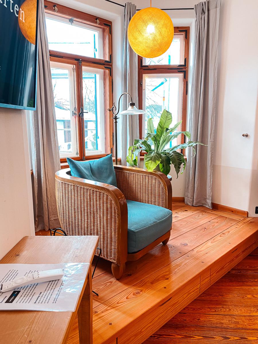 Ein Sessel mit blauem Kissen steht auf einer Holzplattform vor Fenstern mit Vorhängen.