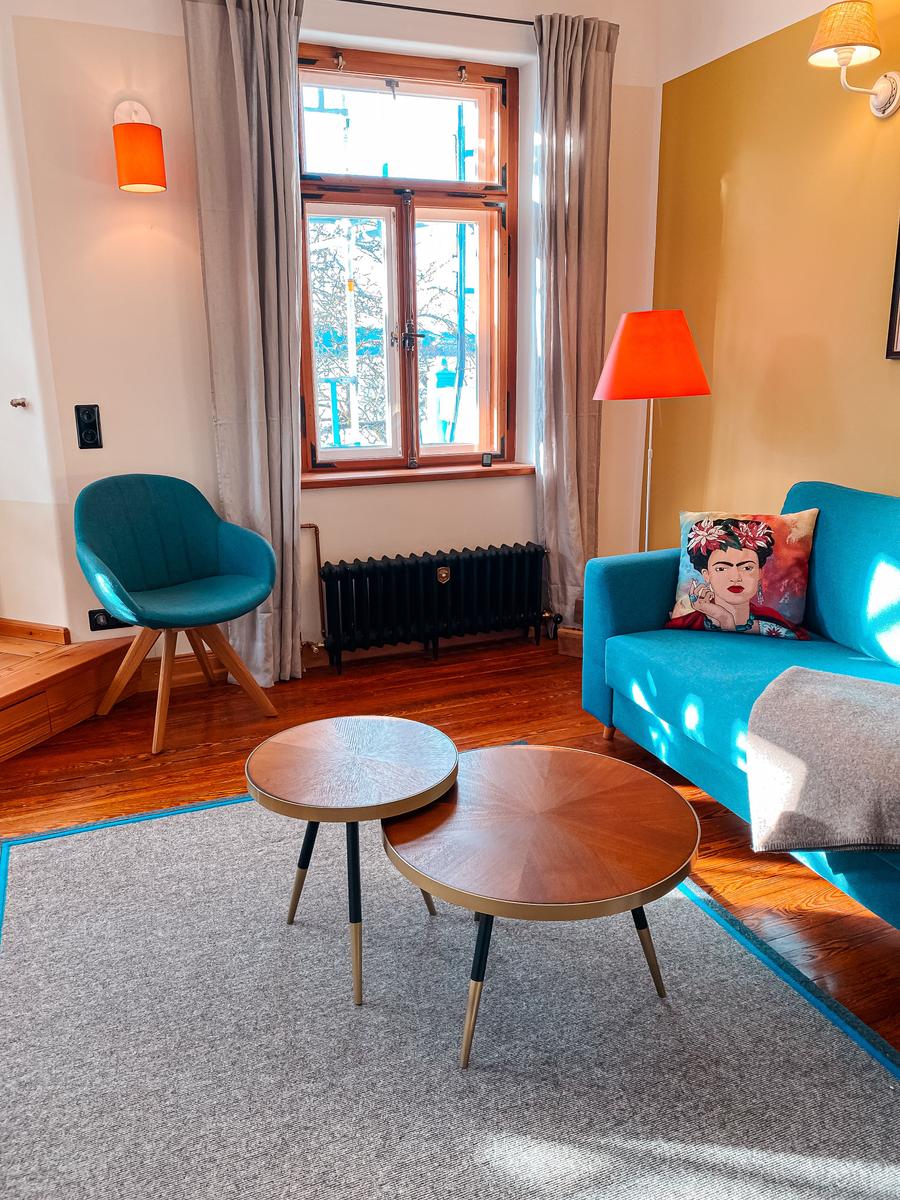 Ein Wohnzimmer mit blauem Sofa, Stuhl und zwei runden Tischen auf Teppich.