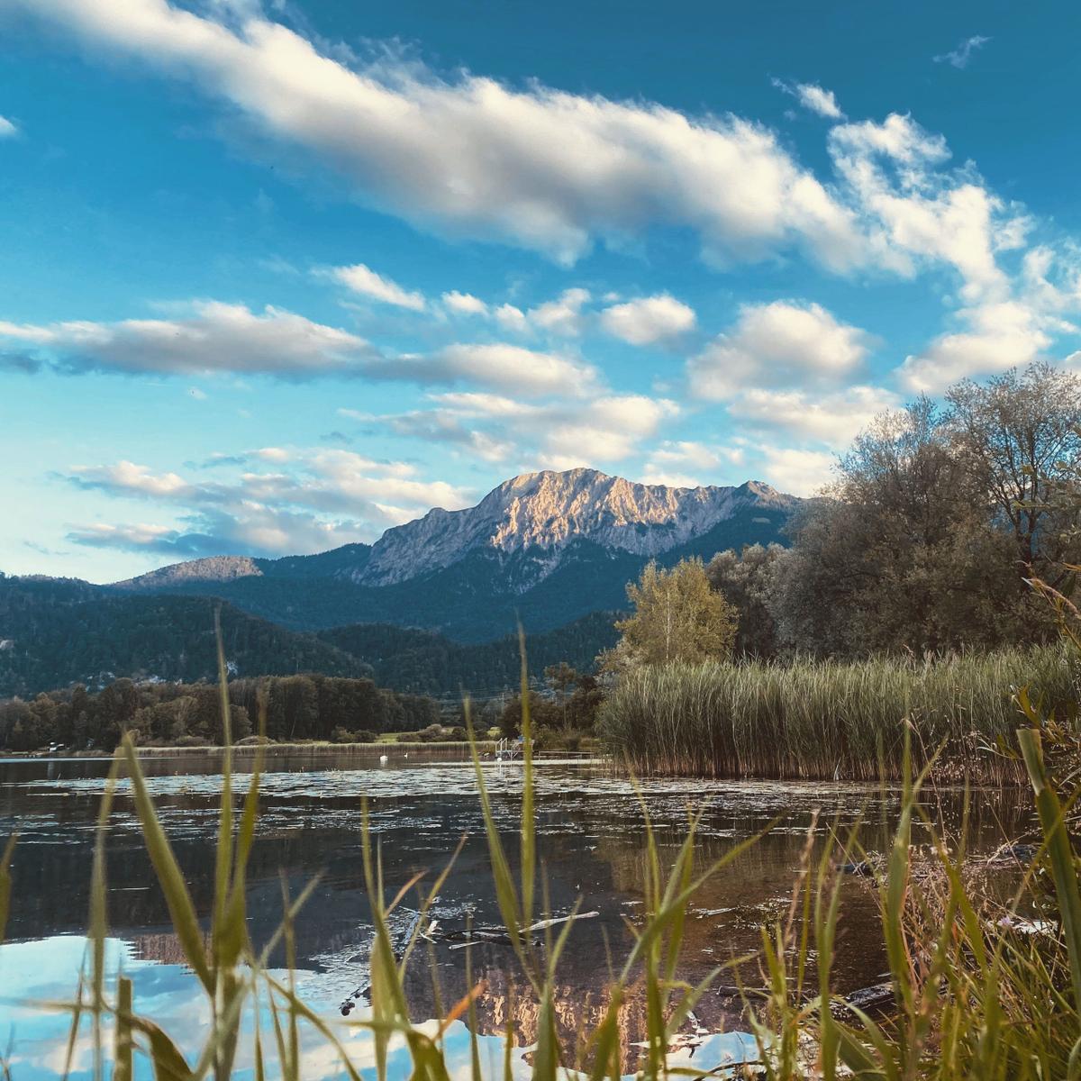 See mit Schilf und Bergen unter blauem Himmel mit weißen Wolken.