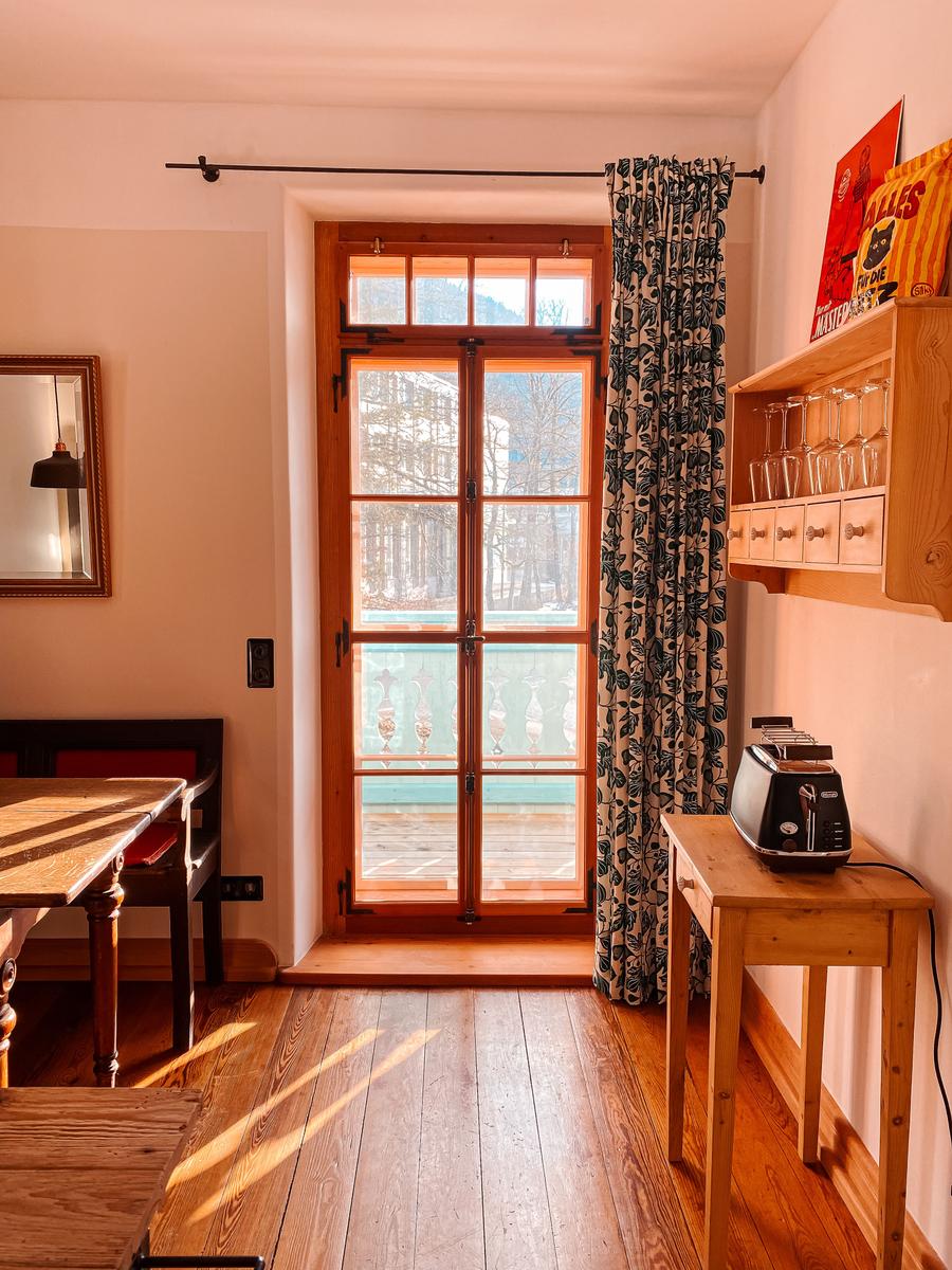 Raum mit Holzboden, Fenster zum Balkon und Küchenmöbel.