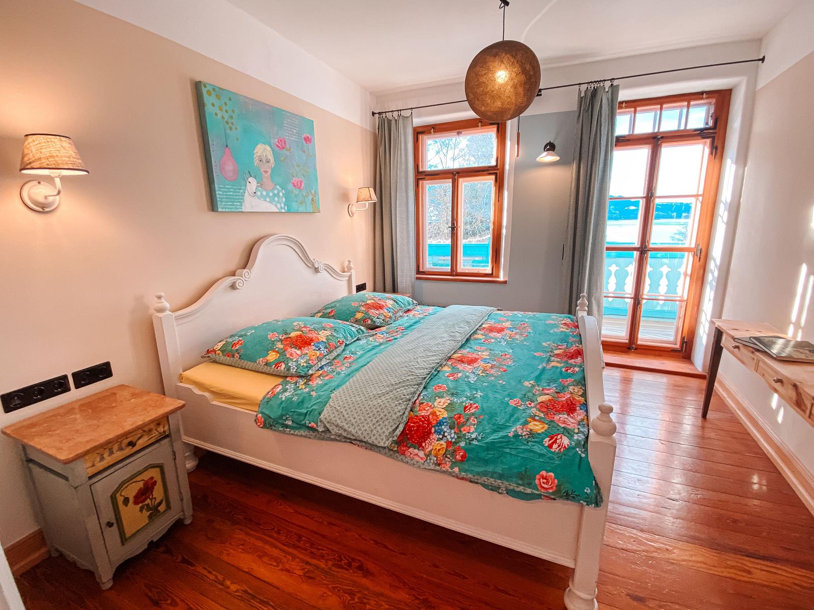 Schlafzimmer mit Bett, Fenster und Holzboden. An der Wand hängt ein Gemälde.