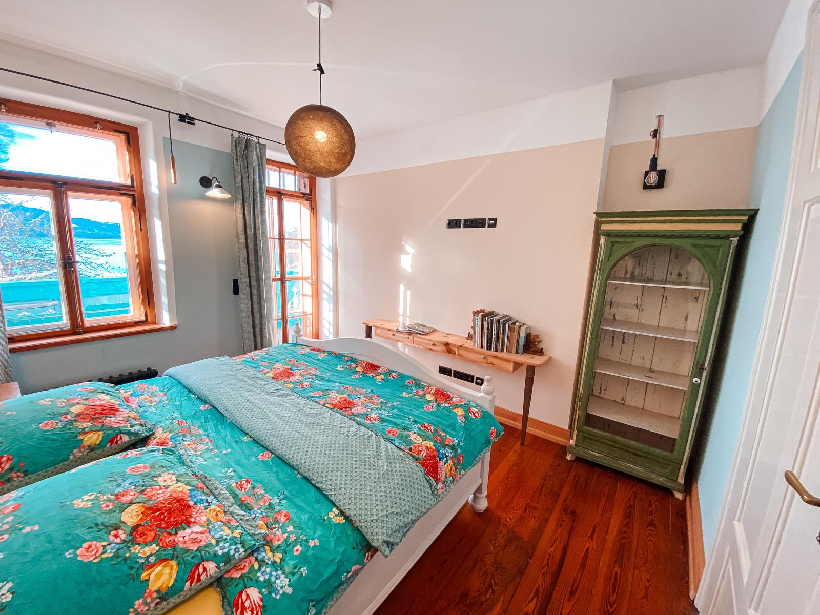 Schlafzimmer mit Doppelbett, Holzboden und Fenster mit Blick auf Wasser.