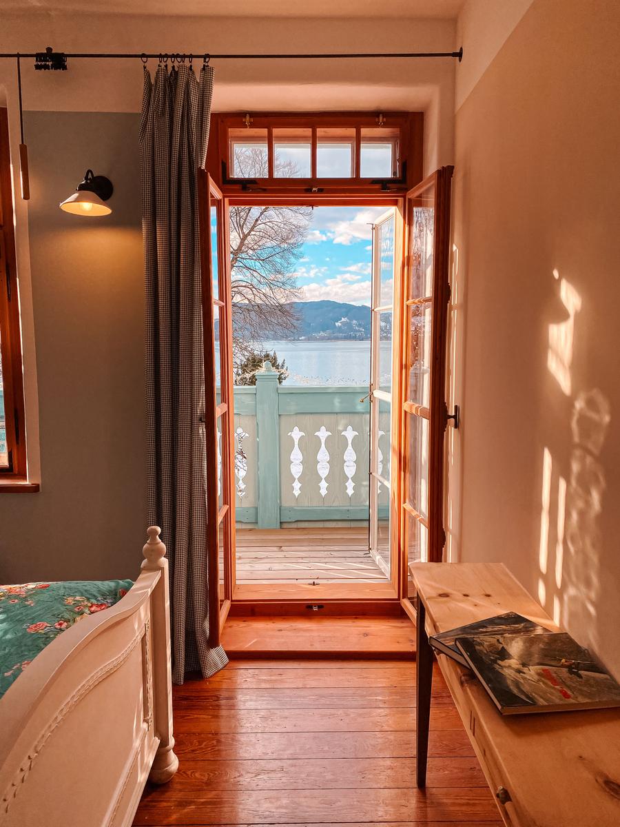 Schlafzimmer mit Blick auf See und Berge durch offene Balkontür.