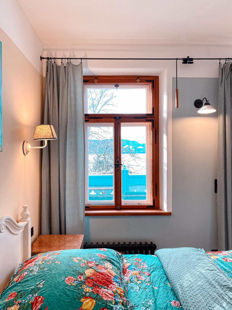 Schlafzimmer mit Fenster, Vorhängen und Bett mit floraler Bettwäsche.