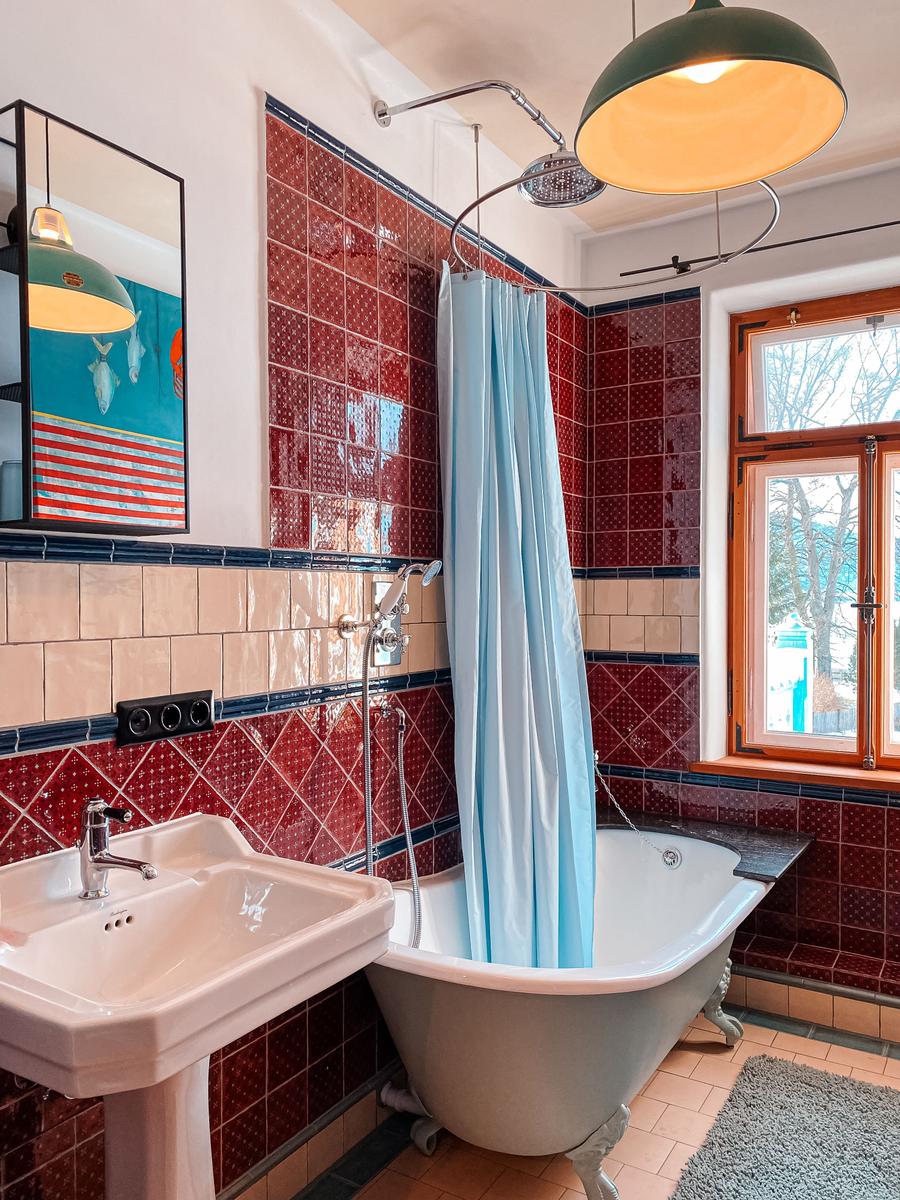 Bad mit freistehender Badewanne, Duschvorhang und roten Fliesen.