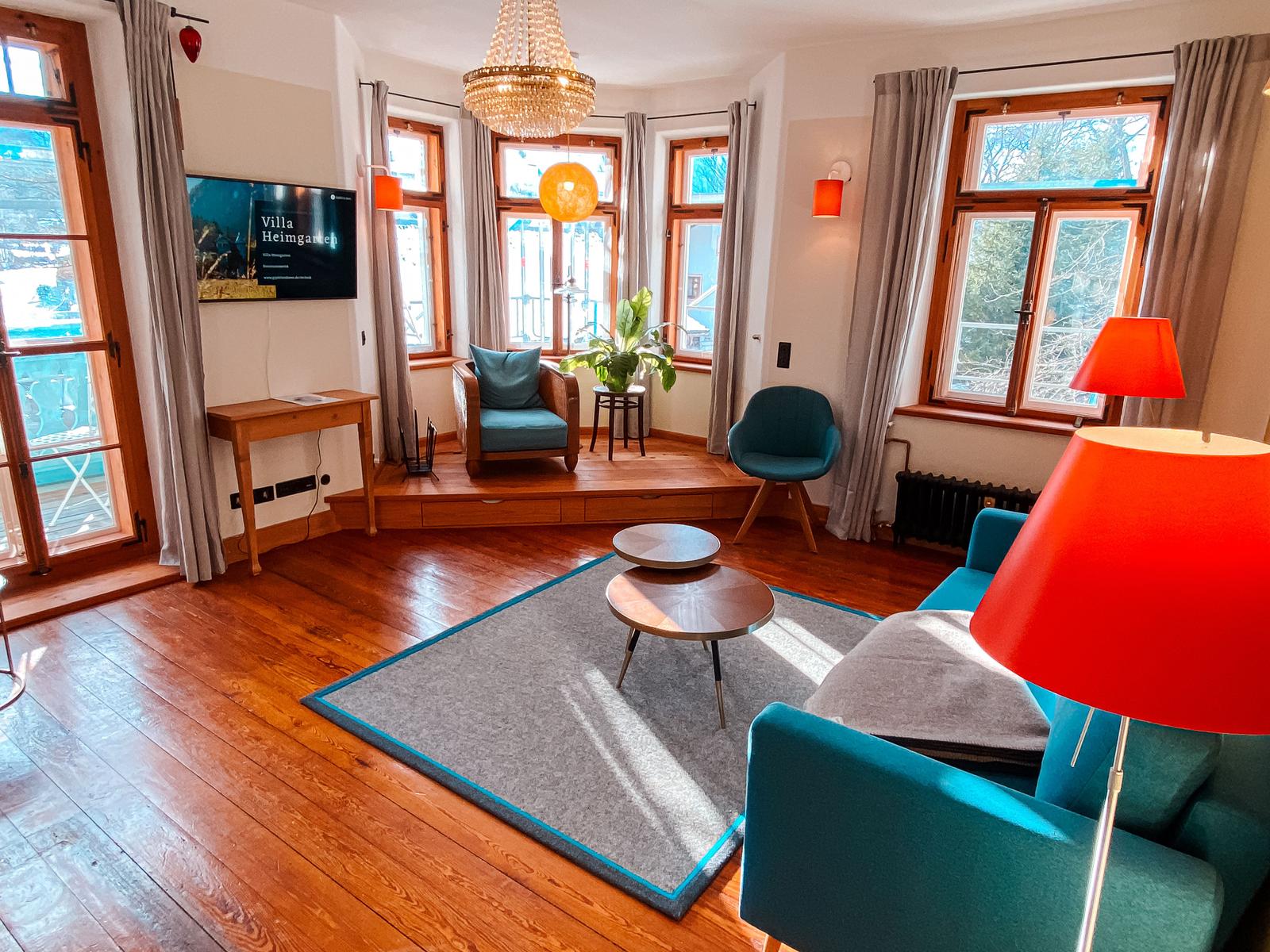 Wohnzimmer mit Holzboden, blauen Sitzgelegenheiten und großen Fenstern.