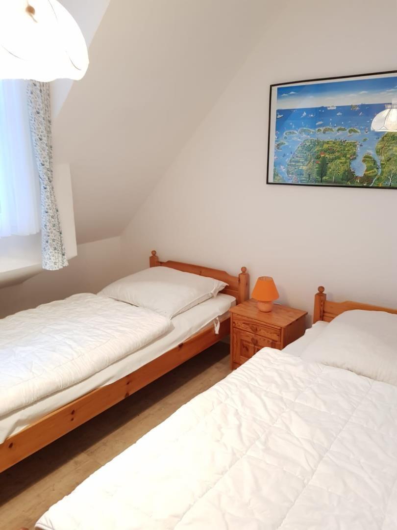 Two single beds with wooden frames and white bedding. Between them stands a nightstand with a lamp.