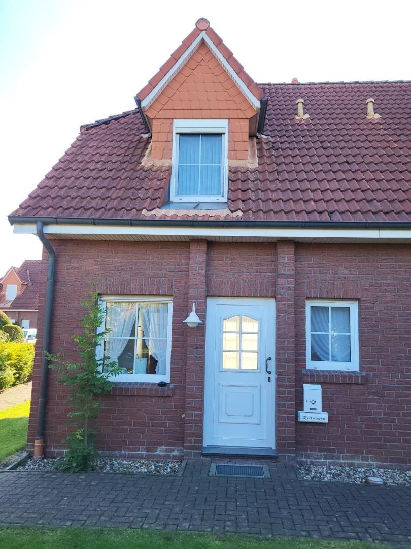 Red tiled roof, white door and windows. House with paved front garden.