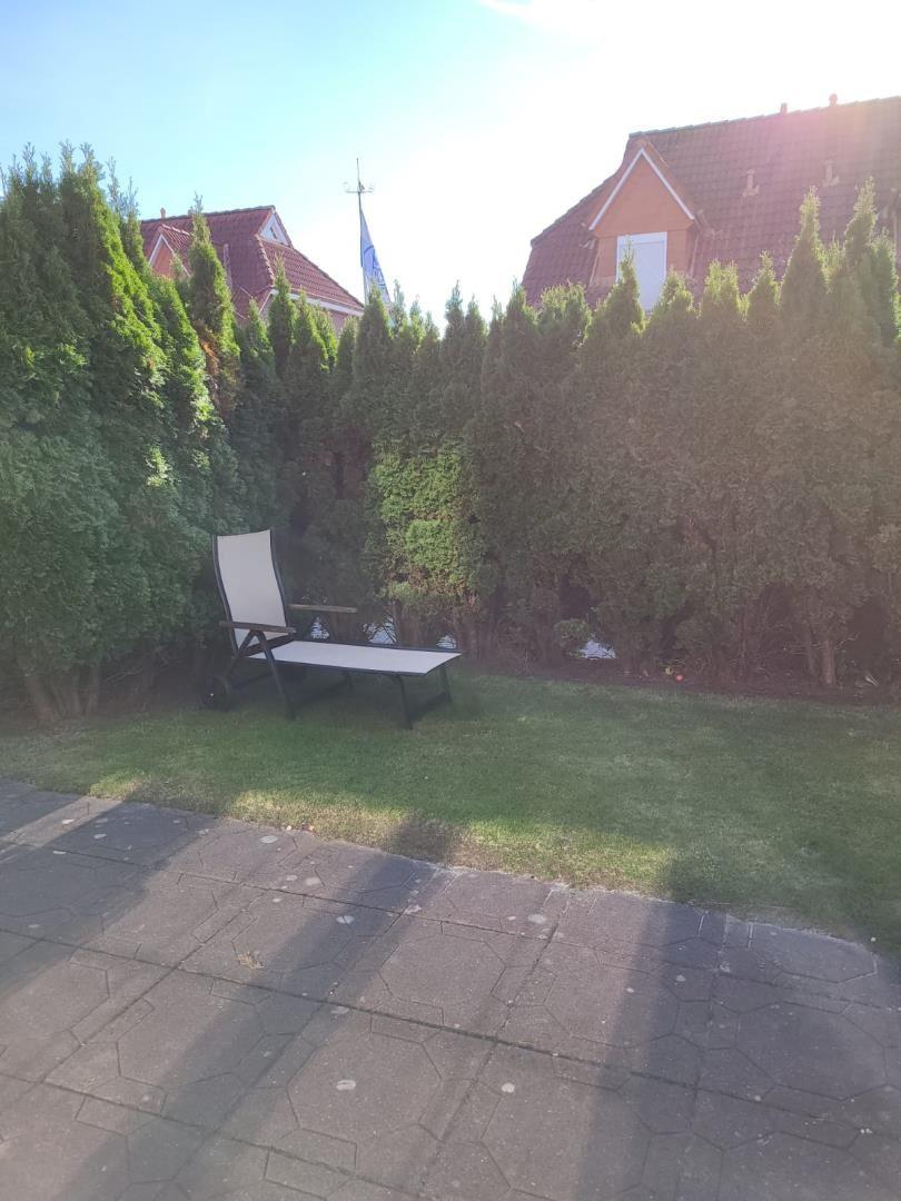 Garden with lounge chair, lawn, and hedges. Background: houses with roofs.