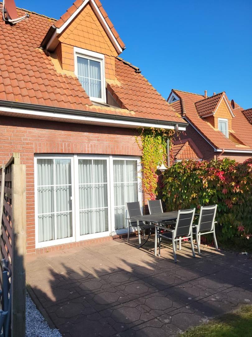 Terrace with table and chairs in front of a house with red roof and climbing plants.