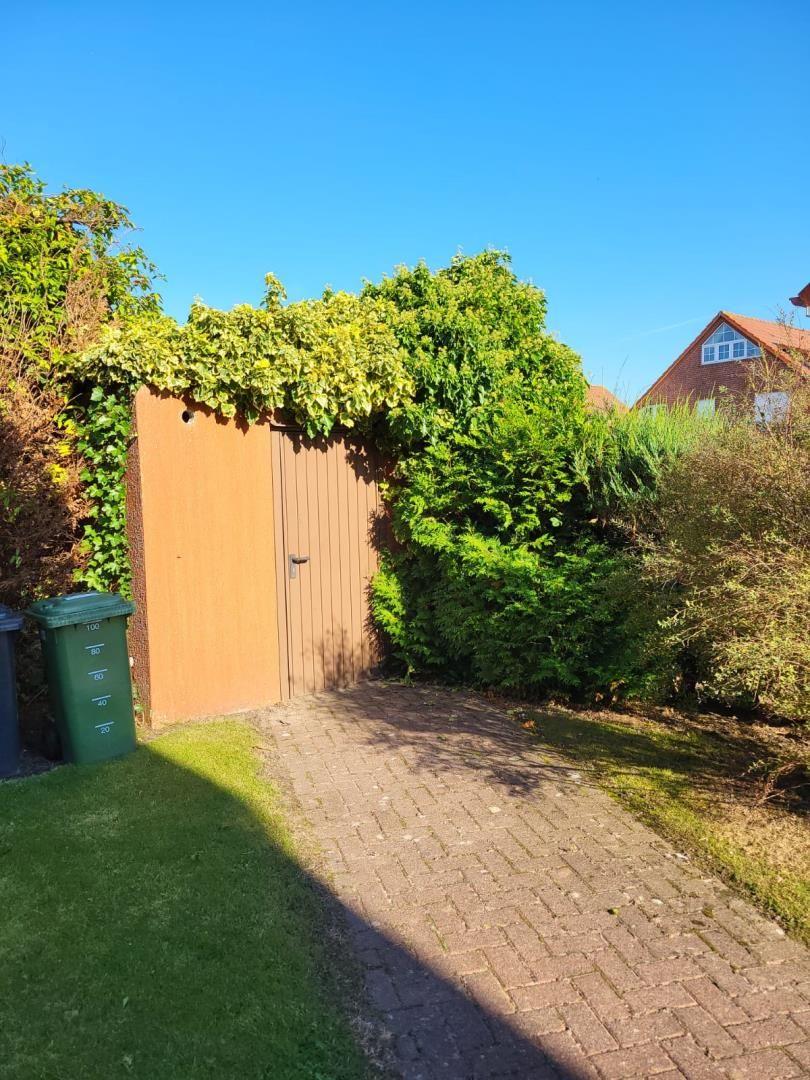 Paved path leads to a wooden door. Surrounded by green areas and shrubs.