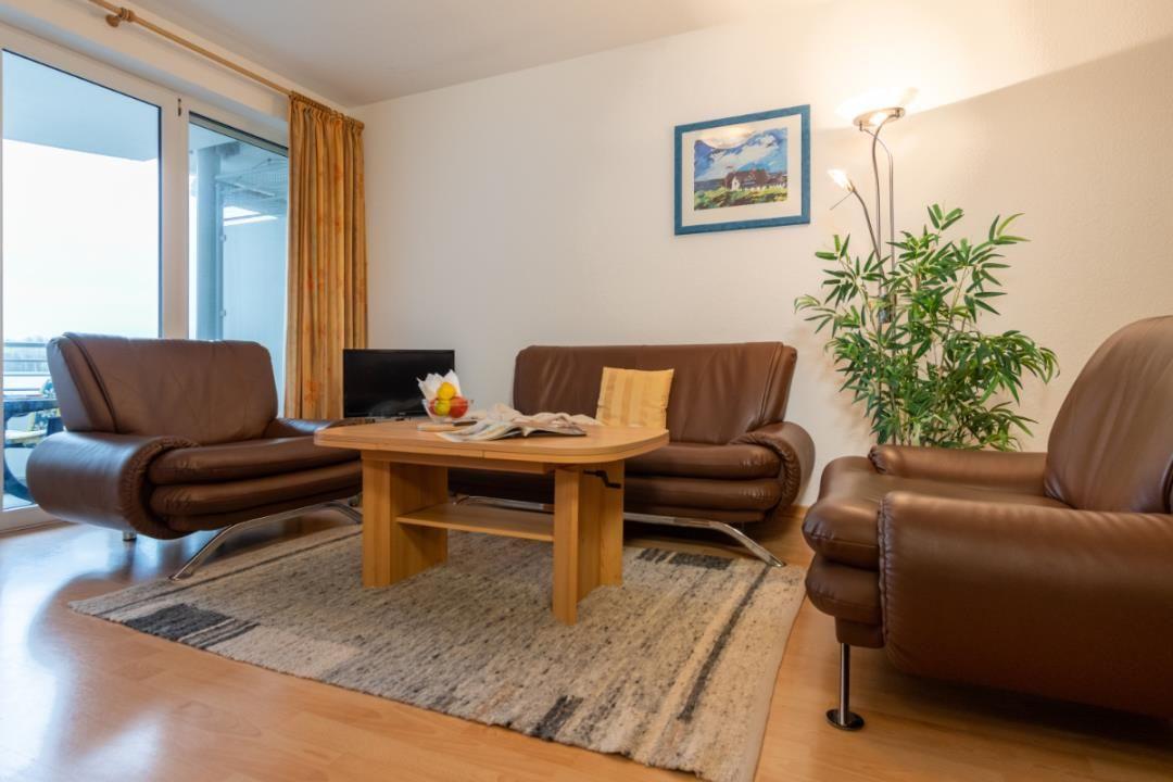 Wohnzimmer mit braunen Ledermöbeln, Holztisch und großem Fenster.