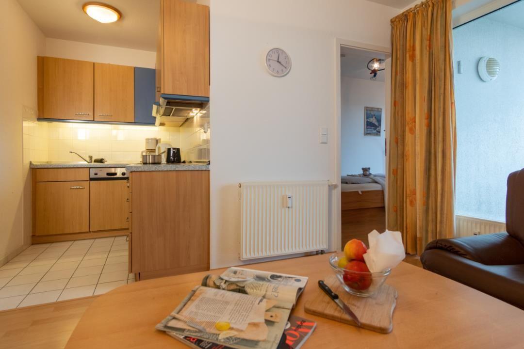 Küche mit Holzschränken, Essbereich mit Tisch und Stühlen, Blick in Schlafzimmer