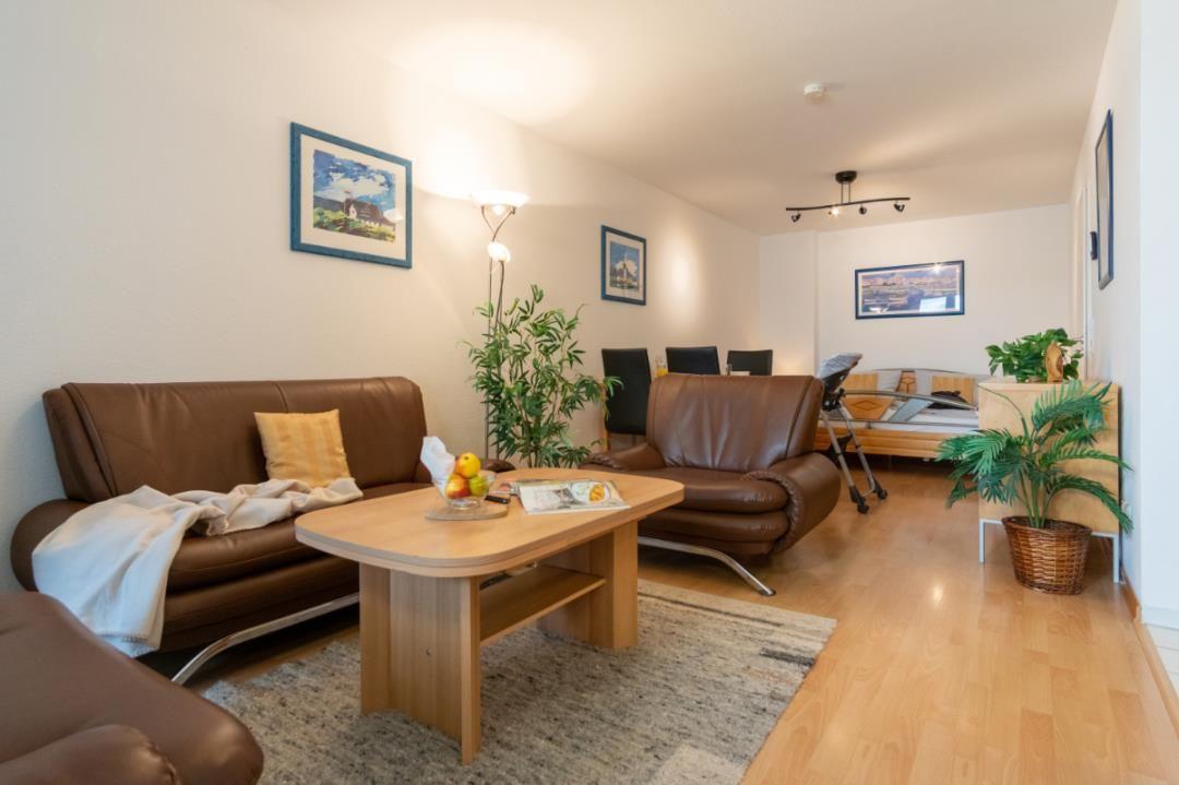 Wohnbereich mit braunen Ledersofas, Holztisch und Pflanzen. Im Hintergrund steht ein Bett.