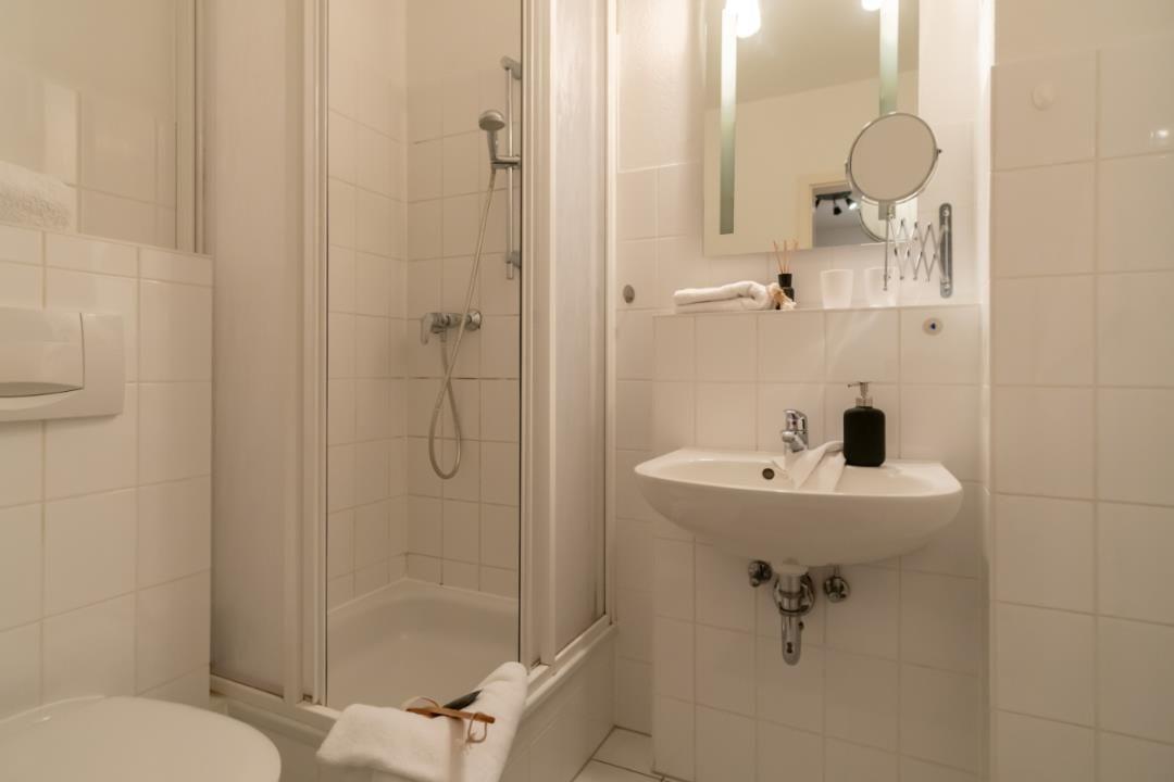 Badezimmer mit Dusche, Waschbecken und Toilette. Weiße Fliesen und Spiegel.