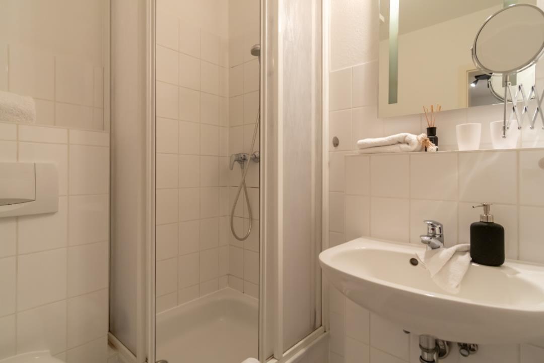 Bad mit Dusche, Waschbecken und Spiegel. Handtuch und Seife sind vorhanden.