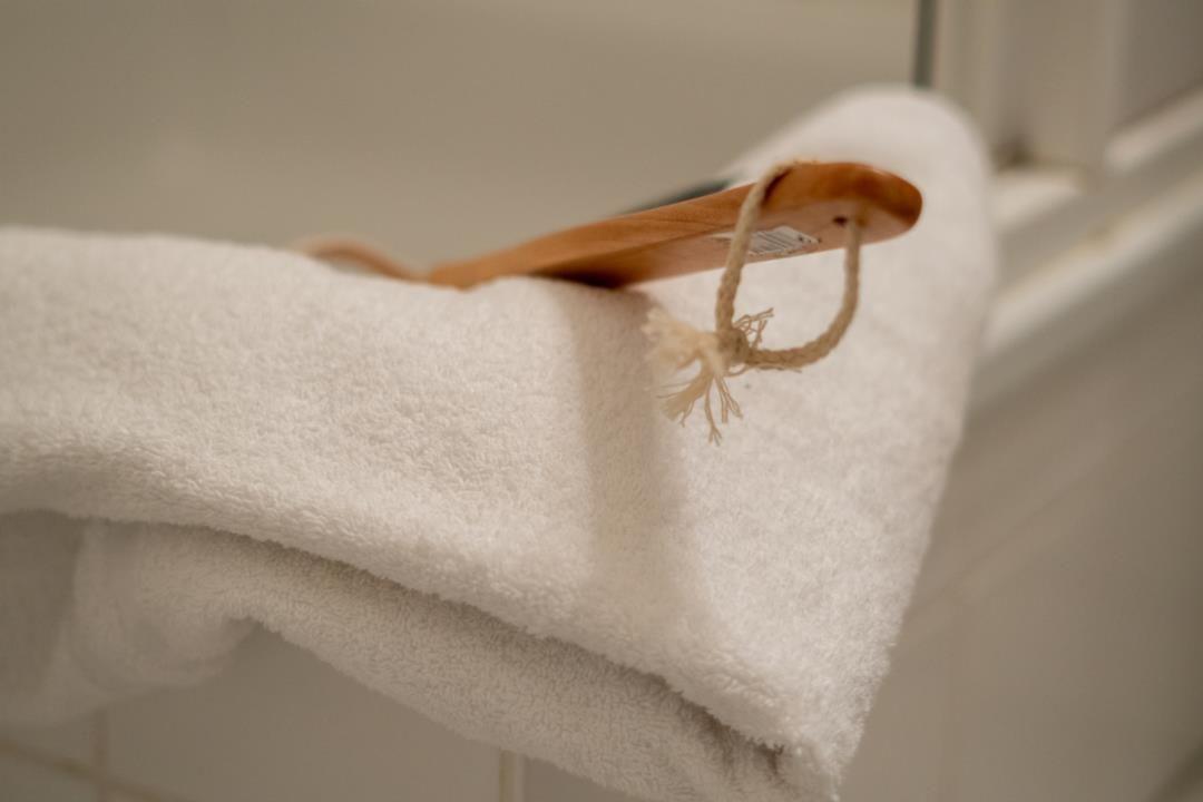 Ein weißes Handtuch liegt gefaltet auf einer Fläche, darauf ein hölzerner Körbchenhalter mit Seil.
