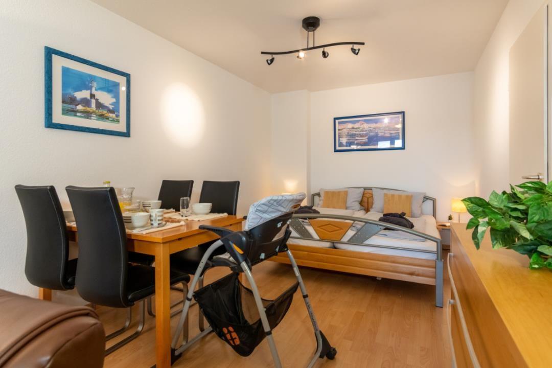 Schlafzimmer mit Bett, Esstisch und Stühlen. Wandbilder und Pflanze sind sichtbar.