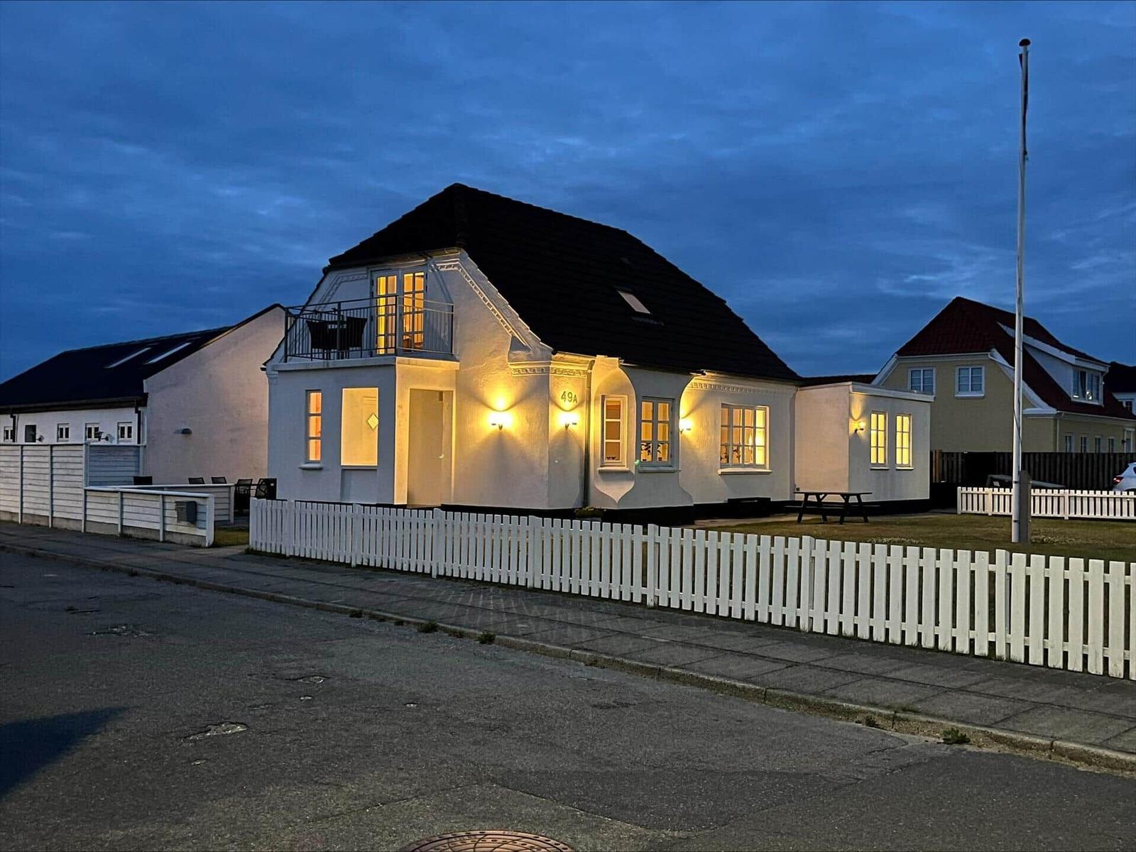 House with white facade, white fence, and lit windows at dusk.