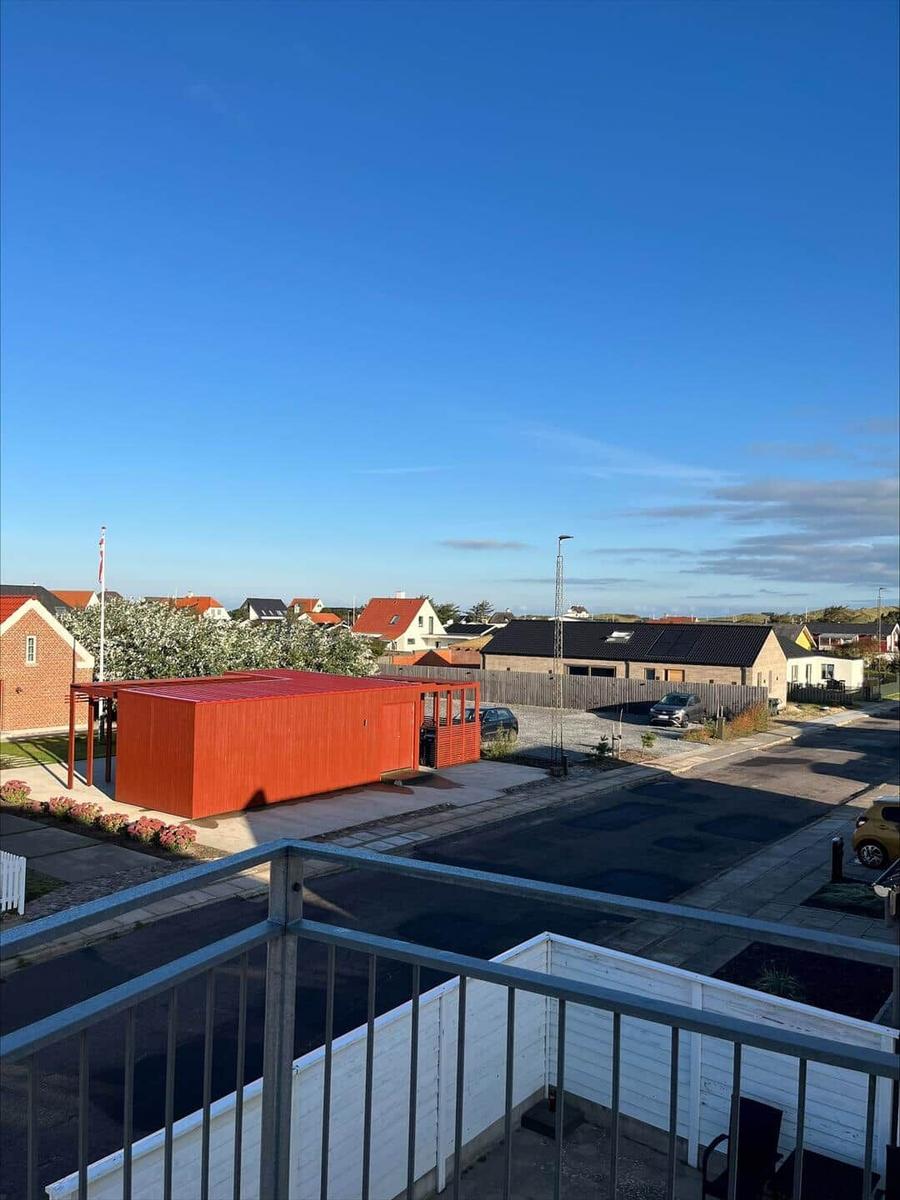 View from balcony over a street with a red container and houses under blue sky.