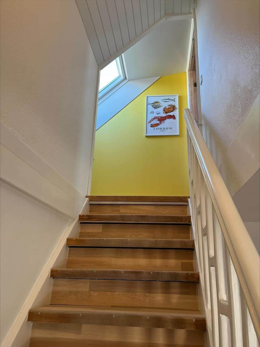 Wooden staircase with white railing and yellow wall with fish picture.