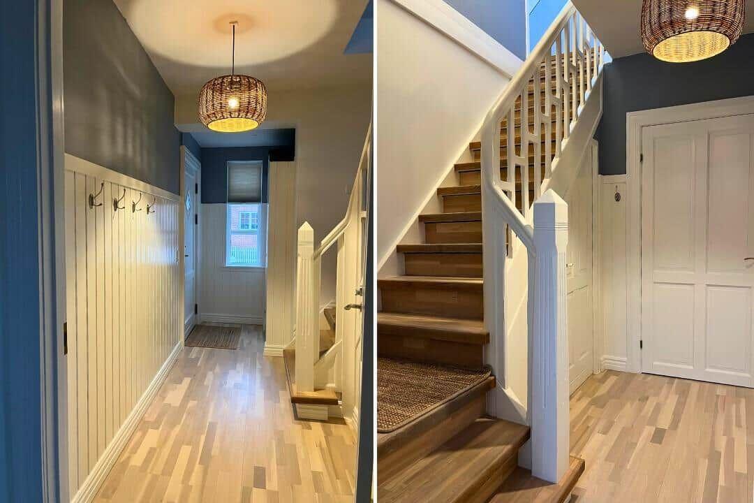 Hallway with wooden staircase and pendant light. Paneling and door visible.