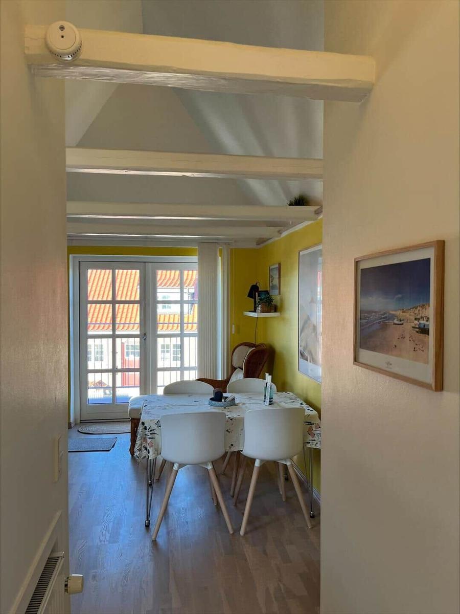 Dining room with table, chairs, and view to balcony. Yellow walls and wooden beams on ceiling.