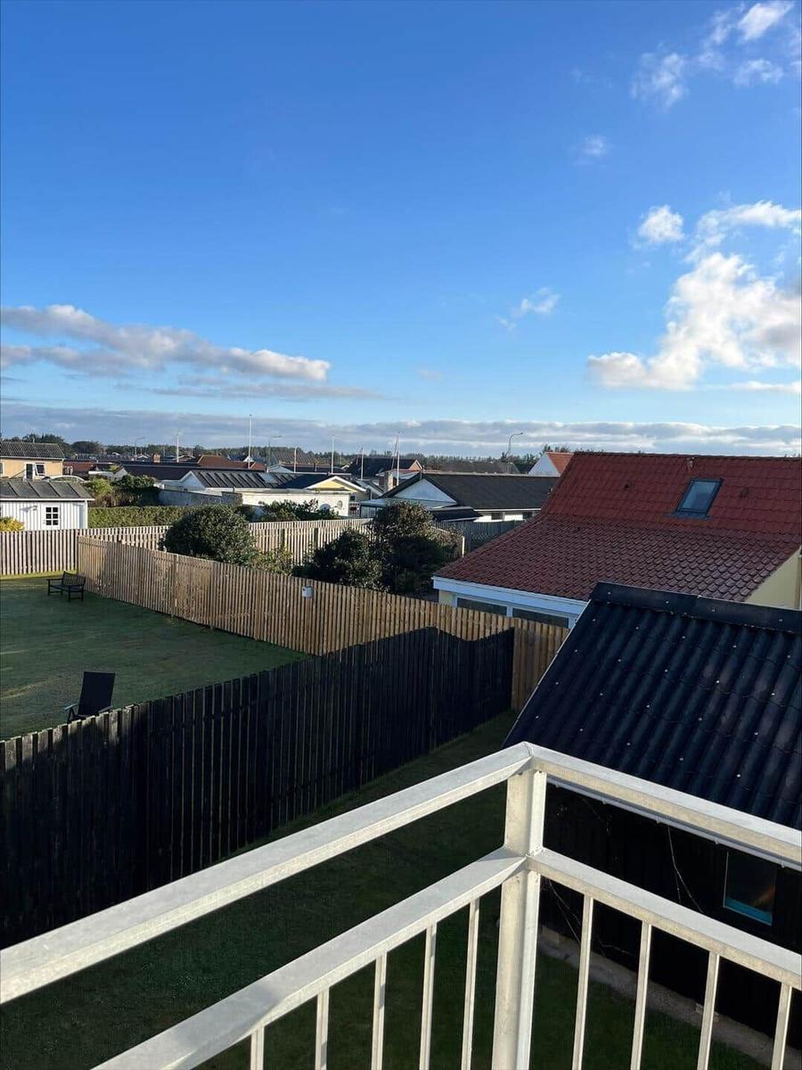 Balcony view over rooftops and green lawn with wooden fences under blue sky.