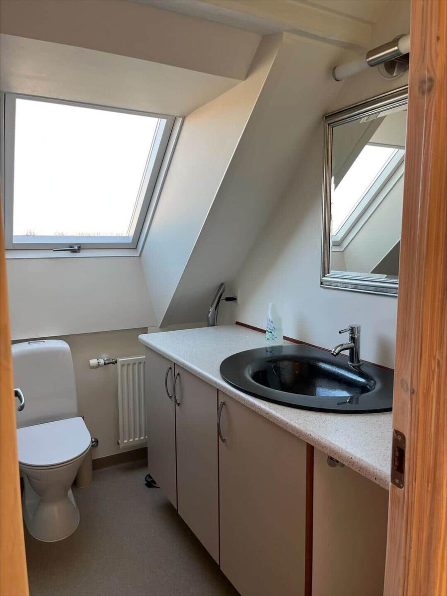 Bathroom with sloped ceiling, sink, mirror, and toilet. Window with view outside.