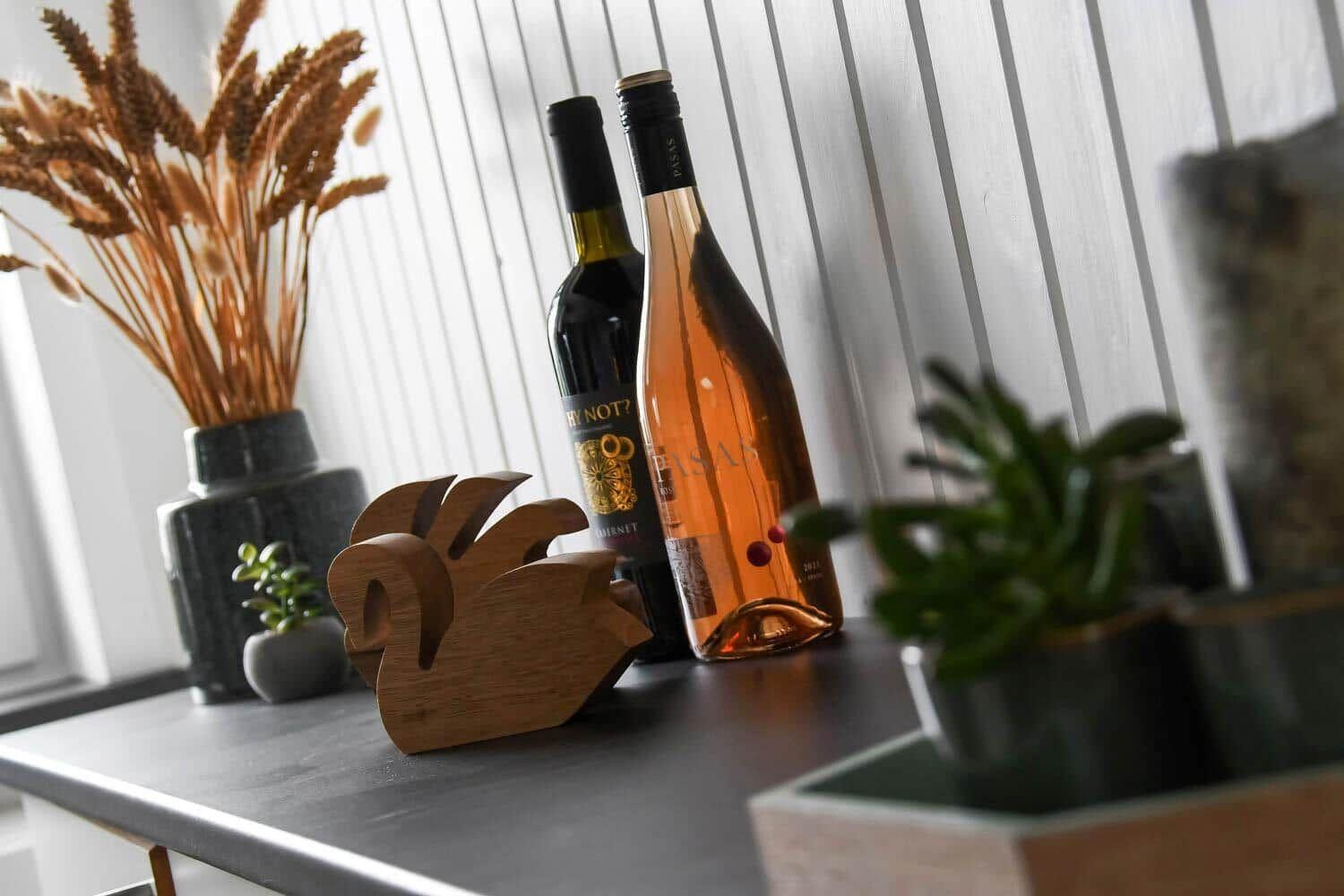 Two wine bottles, a wooden figure, and plants are on the work surface.