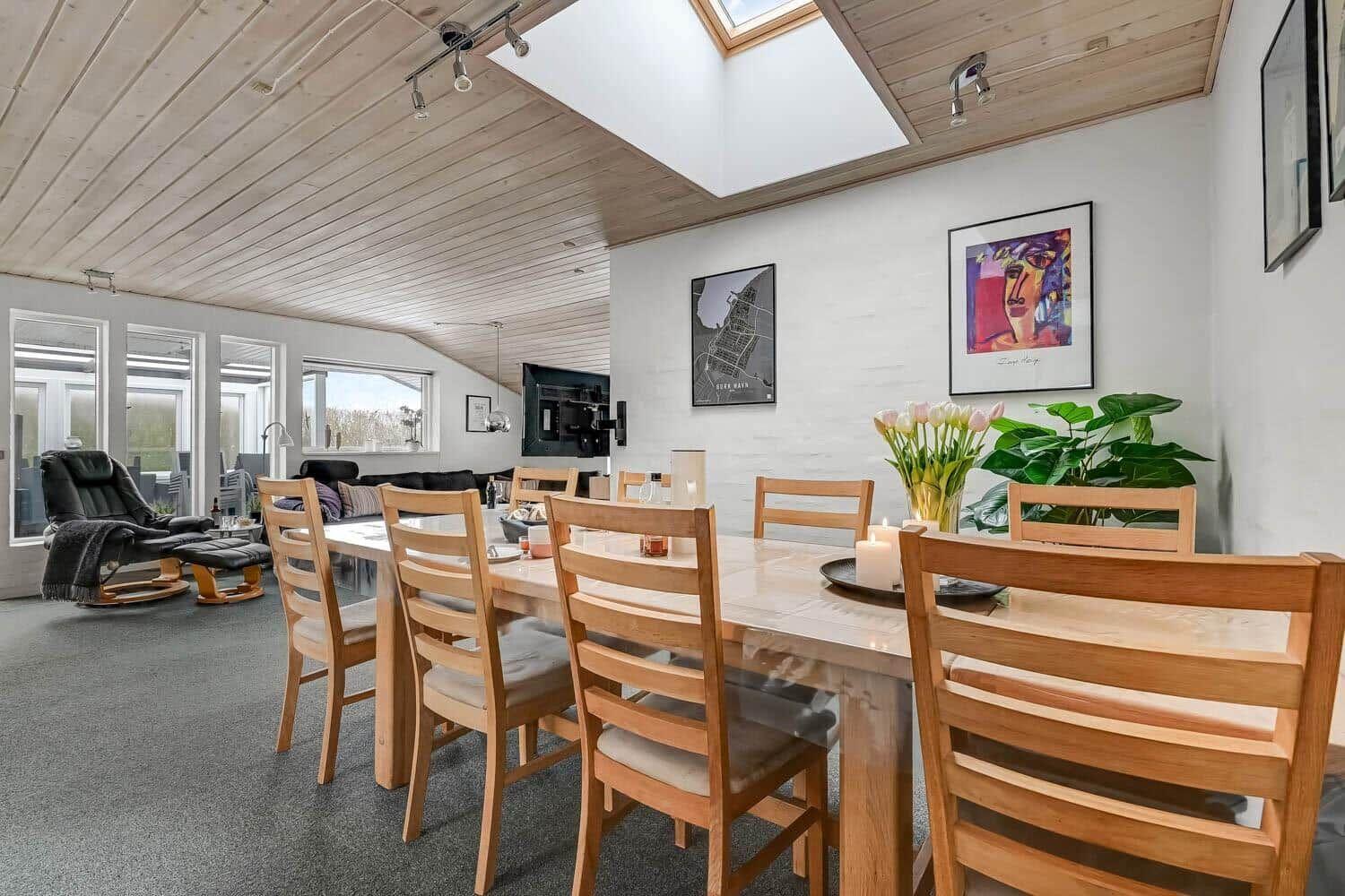 Dining room with wooden table and chairs, wall art, and plants. View into living area with seating.
