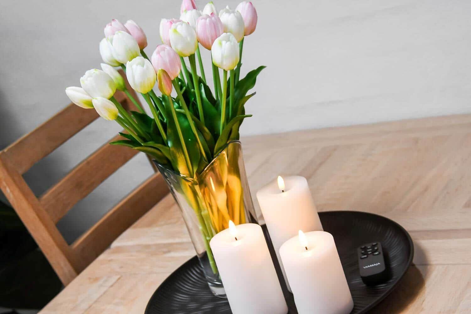 On the table, there are tulips in a glass and three lit candles on a tray.
