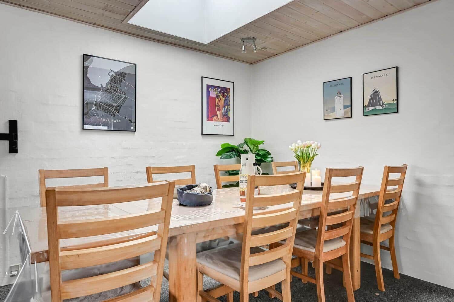 Dining room with wooden table, chairs, and wall art. Ceiling with skylight.