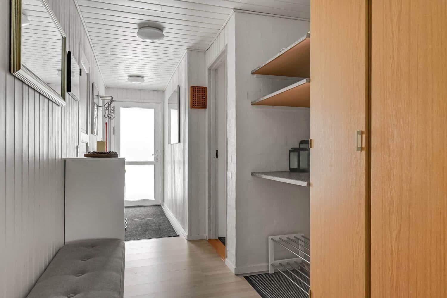 Hallway with wooden floor, white walls, and built-in shelves. Door to outdoor area visible.