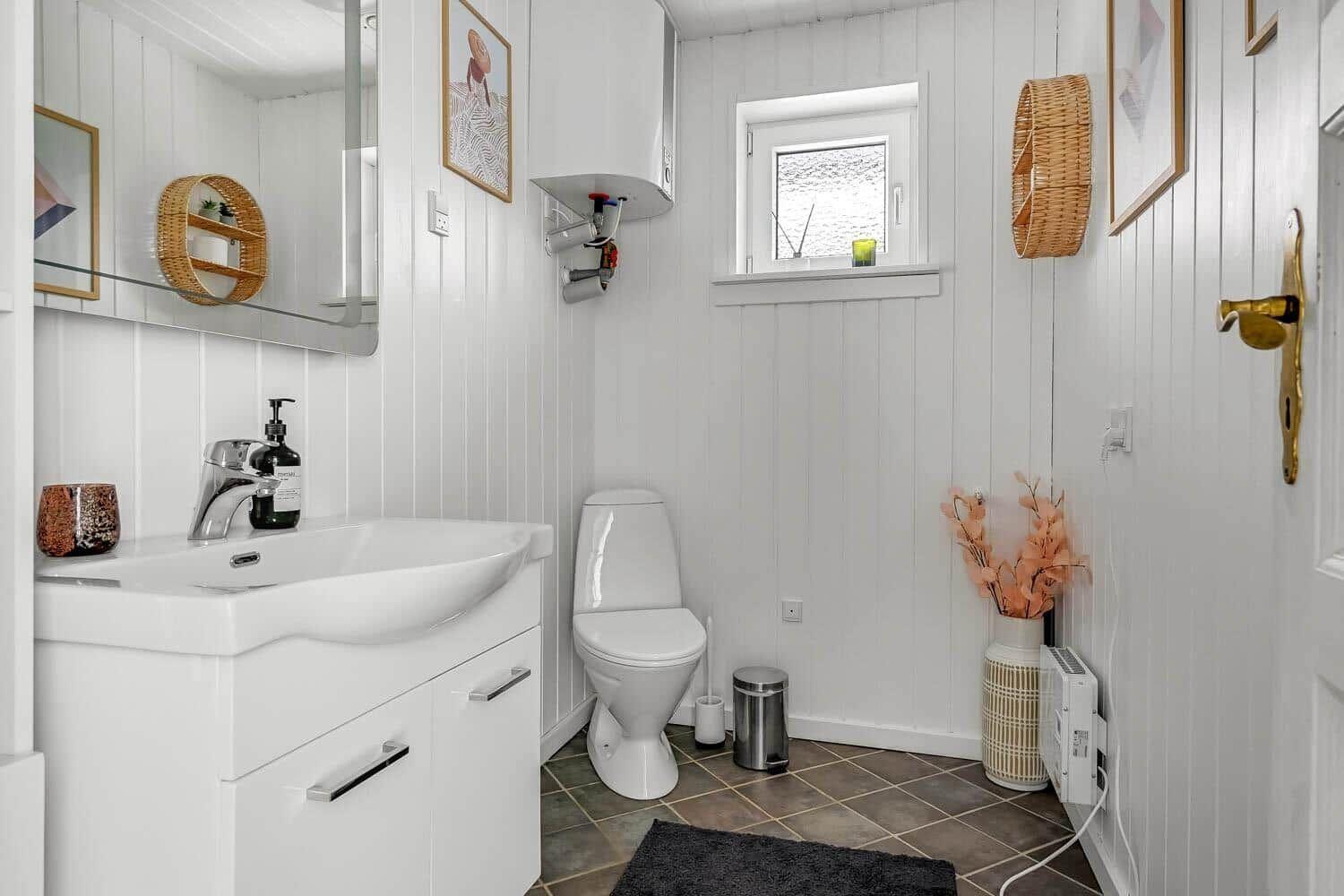 Bathroom with sink, toilet, and window. White walls, brown floor, and decorative items.