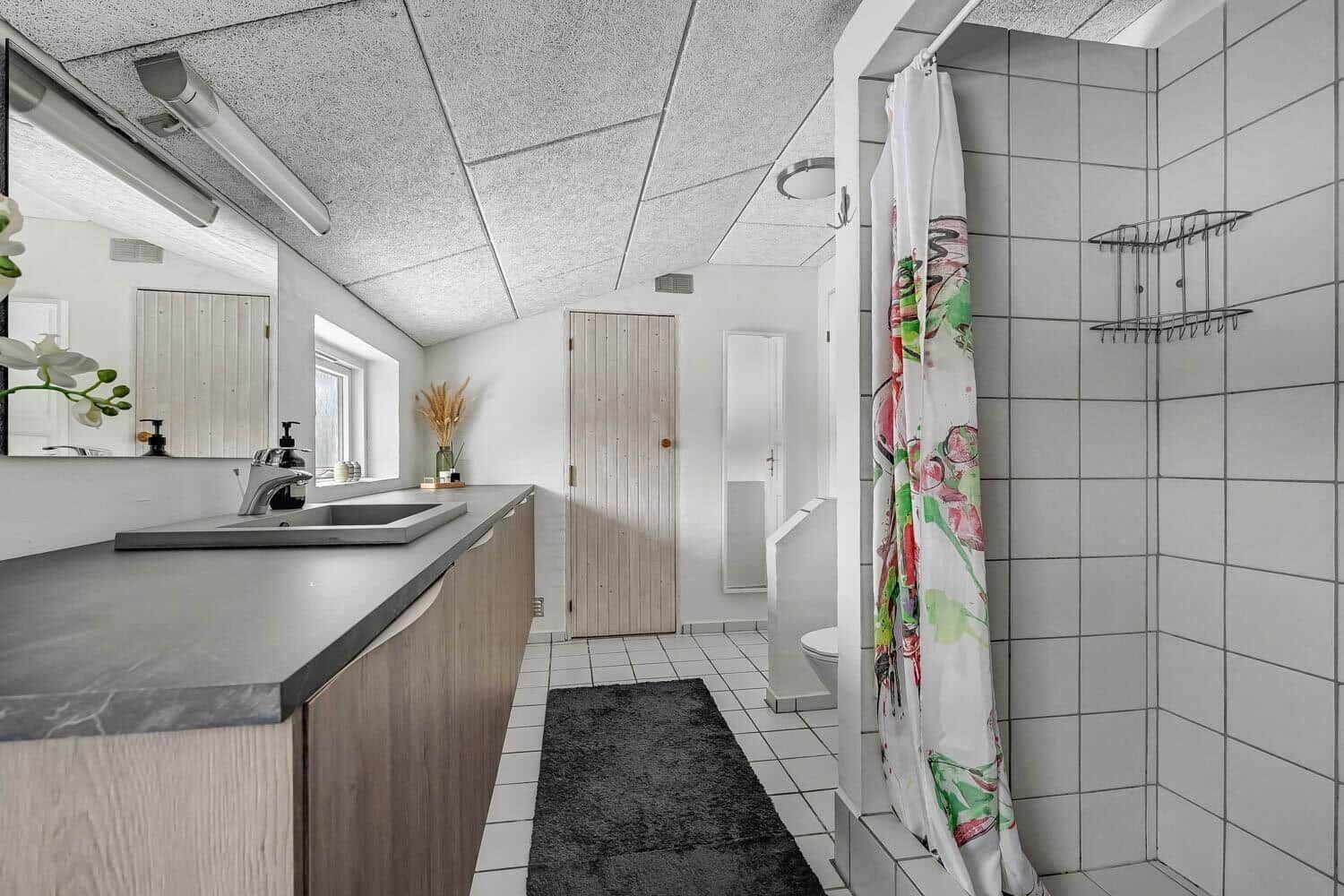 Bathroom with sink, shower, and toilet. Tile floor and wooden cabinets.