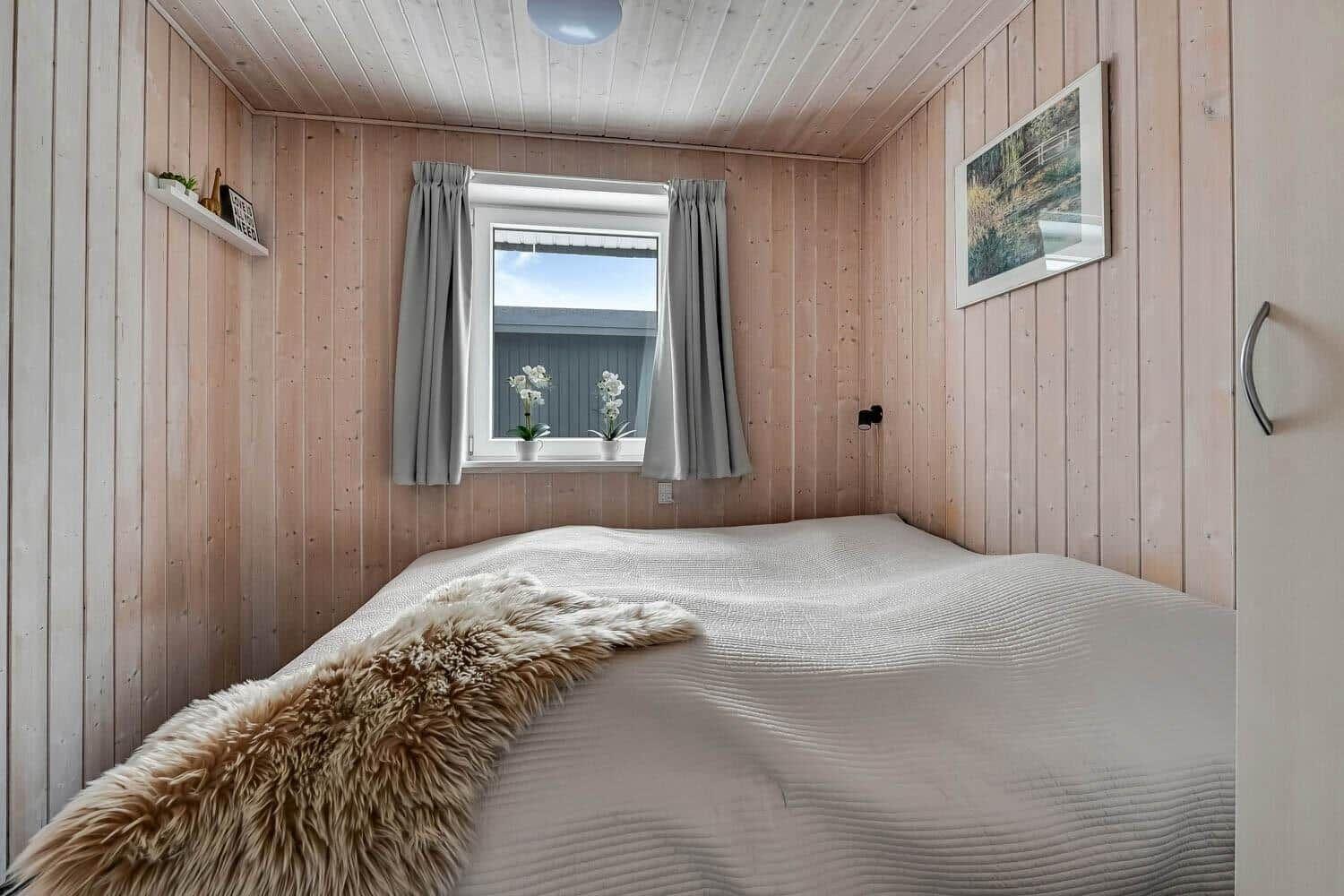Bedroom with wooden walls, window, and bed with fur blanket.