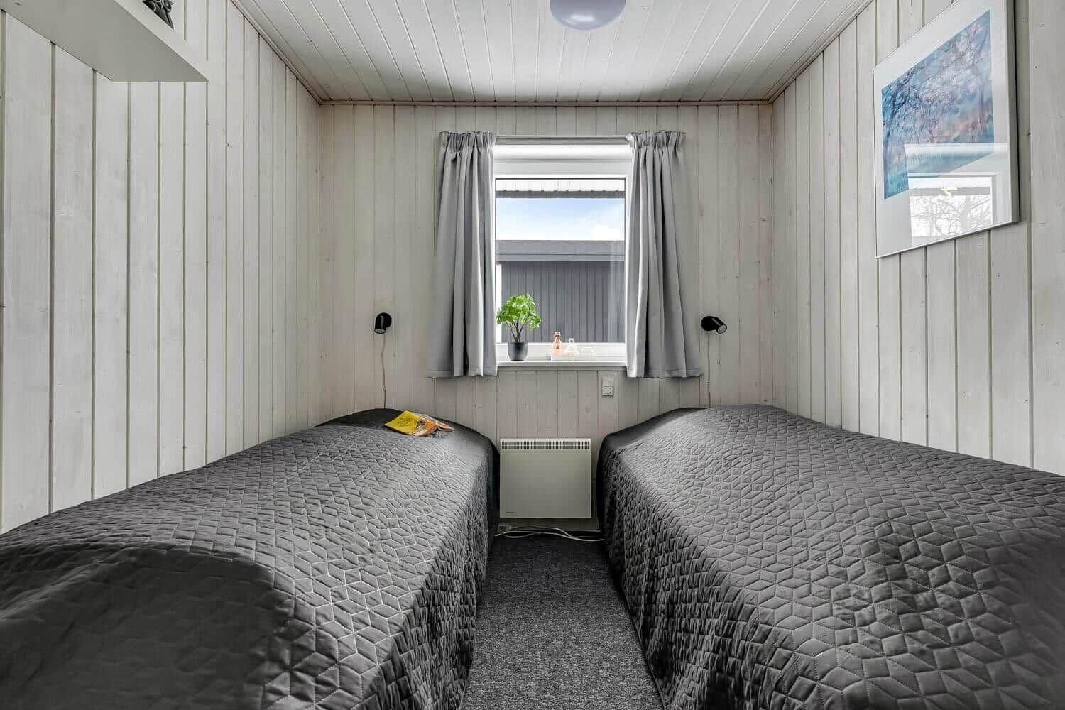 Two beds with gray bedding, window with curtains and wall art.