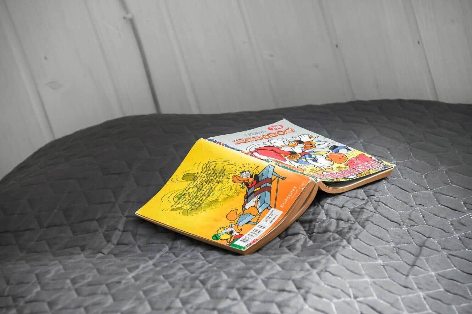 Two comic books rest on a bed with a dark, quilted bedspread.
