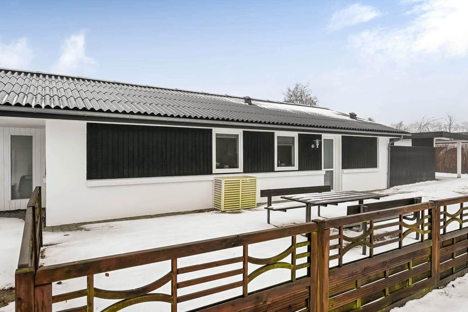House with snow-covered yard, wooden fence, and outdoor table.