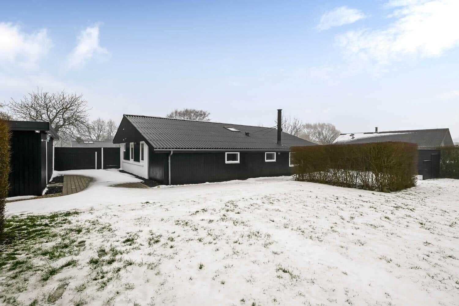 Black house with snow-covered grounds and hedges in winter.