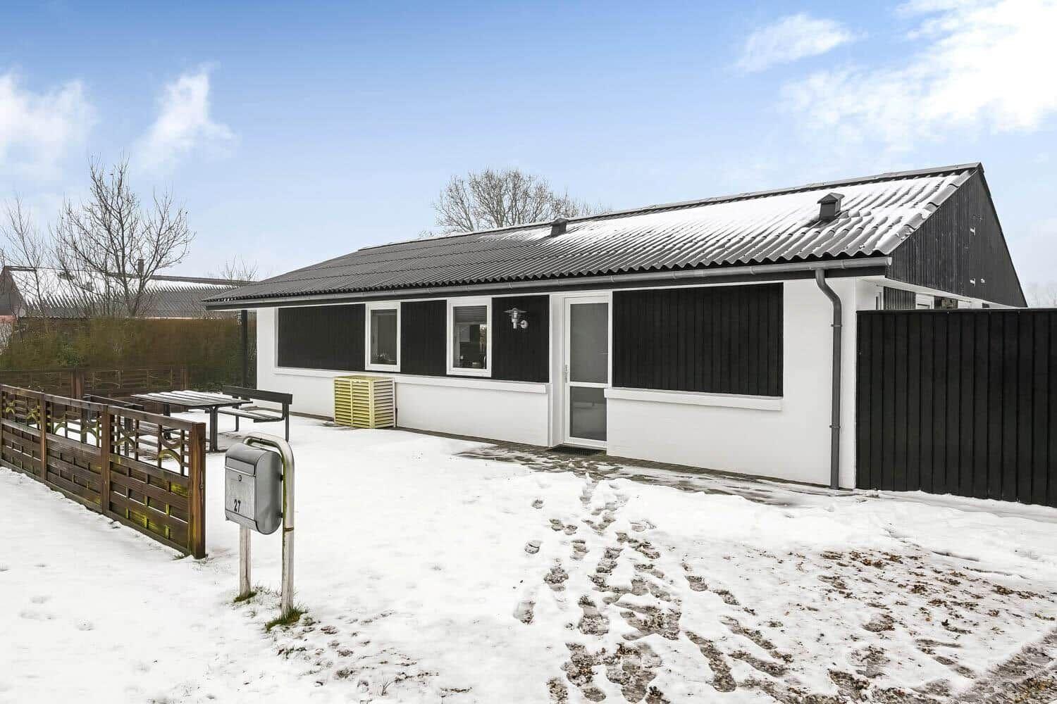A white house with a black roof and shutters stands in the snow.