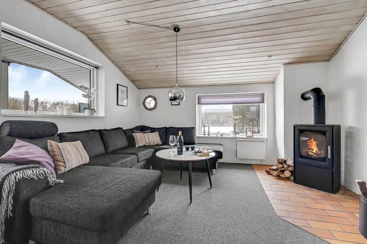 Living room with sofa, fireplace, and windows. Wooden ceiling and carpeted floor.